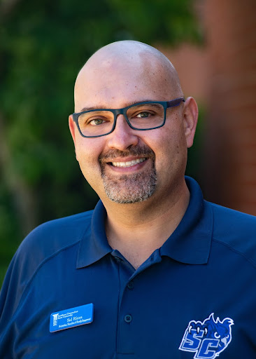 Dr. Sal Rizza of Southern Connecticut State University. He is against a scenic background wearing a blue SCSU polo.