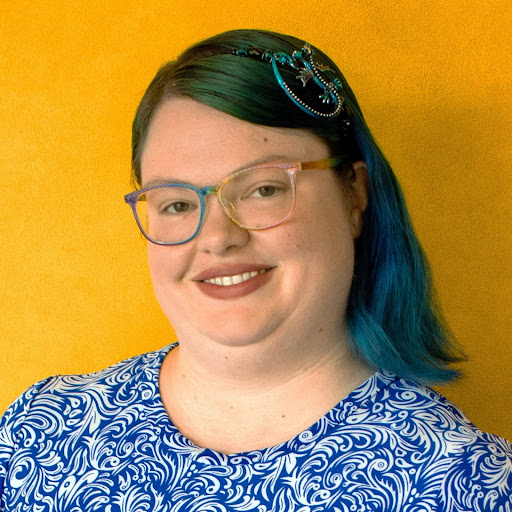 Erin McElroy of the University of Kansas. She is against a yellow background wearing a blue patterned shirt.